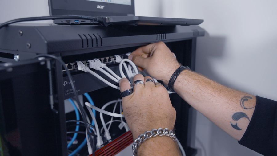 Hände am Patch-Panel mit Switch und Laptop, Patchkabel werden gesteckt